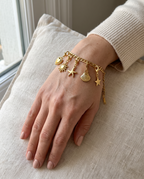 Pulsera Fígaro dorada con charms puesta en la muñeca